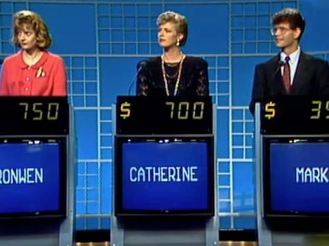 Three contestants stand in a row in a game show setting.