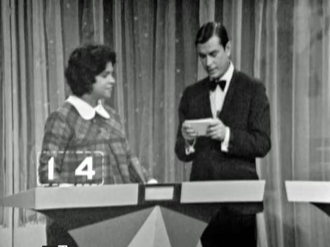 A woman game show contestant stands next to a game show host.