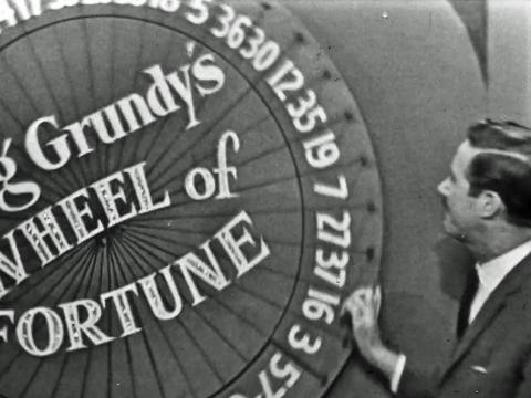 A man is about to spin a large game show wheel that says Reg Grundy's Wheel of Fortune on the front.