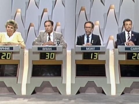 A woman and three men sitting in a row on a tv game show studio set