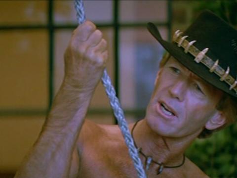 Paul Hogan as Mick Dundee, wearing his trademark akubra hat and holding a rope as he talks to a hitman