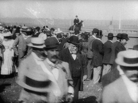 Black and white still of a crowd of people watching the 1896 Melbourne Cup