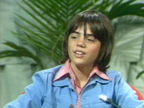 Greg Rowe, wearing a blue jacket and red and white checked shirt, being interviewed on the Mike Walsh show in the studio