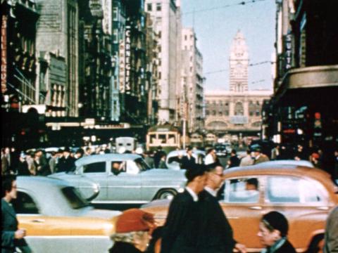 Trams, cars and people in the centre of Melbourne city with Flinders Street railway station in the background