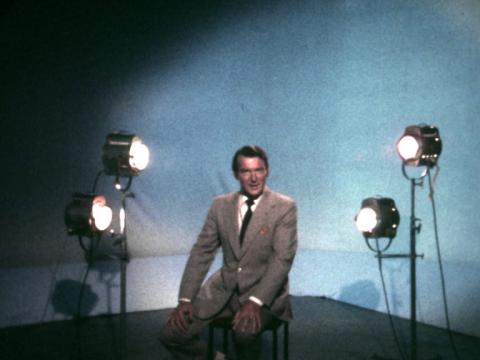 Television personality Roger Climpson sits on a stoll in a studio