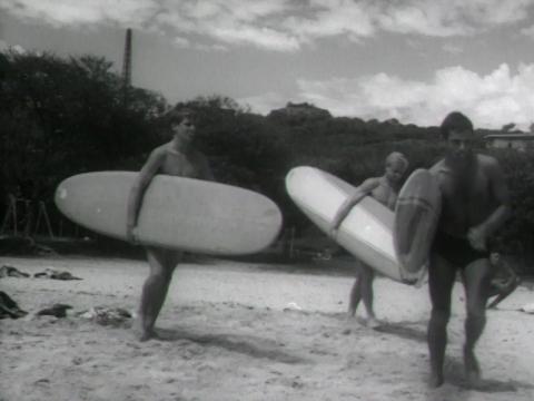 Three young men stand on Manly beach holding surfboards