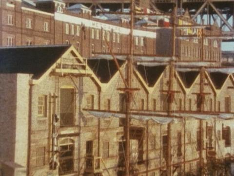 Buildings at The Rocks with the masts of a tall ship in the foreground and the Harbour Bridge in the background