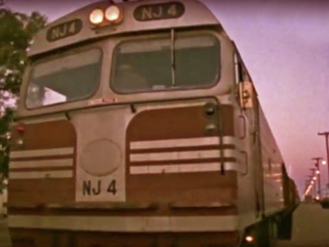 Front of a passenger train pulling up alongside a platform at dusk.