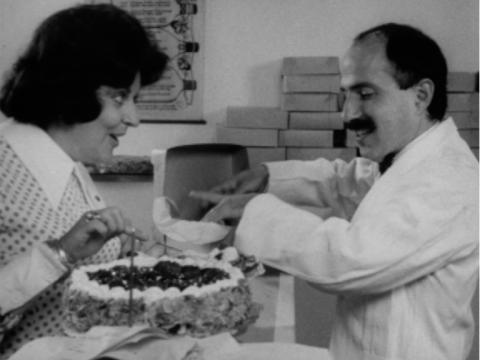 A woman is buying cakes at a French patisserie from a man behind the counter. 