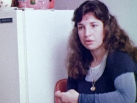 A young Greek woman seated in her kitchen.