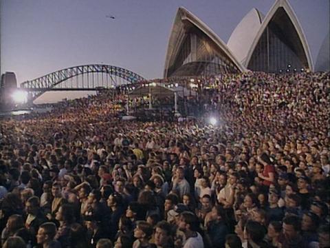 A sea of people cover the forecourt steps of the Opera House. The Sydney Opera House sails and the Sydney Harbour Bridge are in the background.