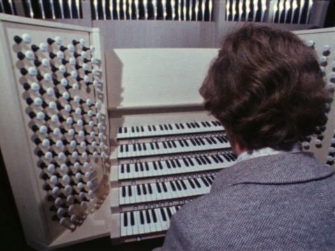 A man is sitting down to play a pipe organ with five keyboards stretching out in front of him.
