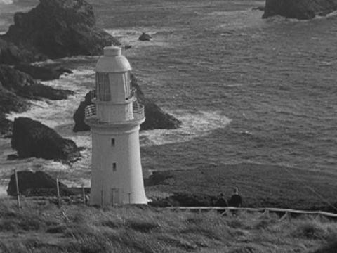 View looking down at a lighthouse, ocean and rocks.