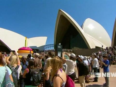 The sails of the Opera House with people in the foreground and a giant cupcake behind them.