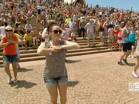A group of dancers dance on the Forecourt and steps of the Sydney Opera House.