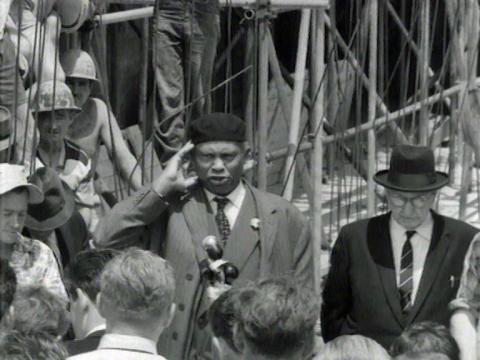 Singer Paul Robeson is singing on a building site. There is a crowd of people around him.