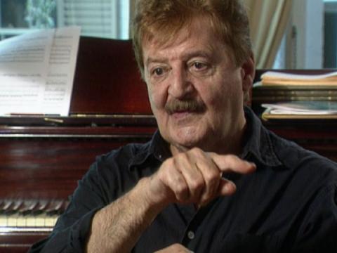 Portrait of Peter Sculthorpe with piano behind him.