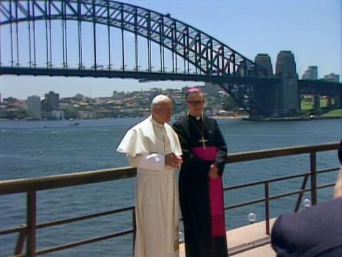 Pope John Paul II is standing with a Catholic Archbishop with the Sydney Harbour Bridge in the background.