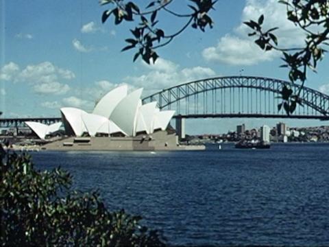Sydney Opera House seen from afar with the Sydney Harbour Bridge in the background. Sydney Harbour is sapphire blue in front.
