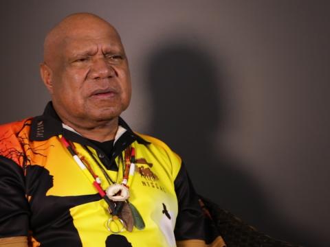 Archie Roach pictured from the waist up, seated and looking slightly away from camera.