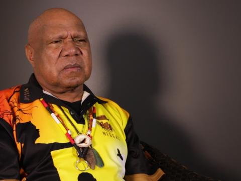 Archie Roach pictured from the waist up, seated and looking slightly away from camera.