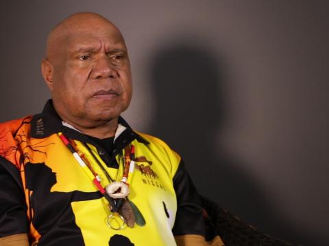 Archie Roach pictured from the waist up, seated and looking slightly away from camera.