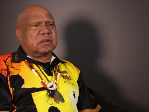 Archie Roach pictured from the waist up, seated and looking slightly away from camera.