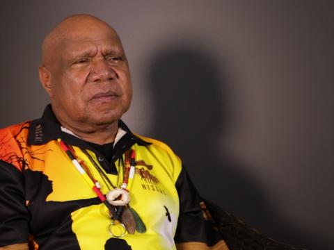 Archie Roach pictured from the waist up, seated and looking slightly away from camera.