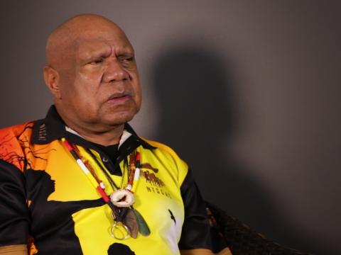 Archie Roach pictured from the waist up, seated and looking slightly away from camera.