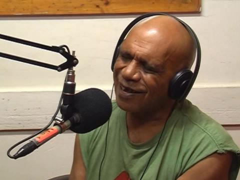 Archie Roach is speaking into a microphone in a radio studio.