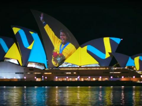 Cathy Freeman holds her hand up in a victory wave after winning a Gold Medal at the Sydney Olympics in 2000. The image is projected onto the sails of the Sydney Opera House.