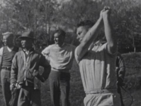 One man teeing off playing golf while others watch