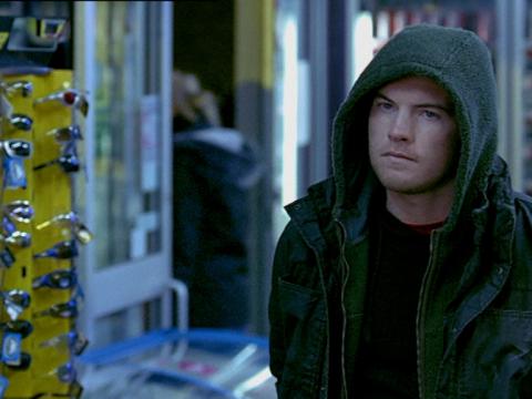 Sam Worthington is looking at someone off camera in a still from Somersault. He is wearing a hoodie and is standing in a service station setting.