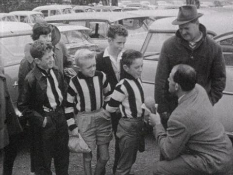 A man interviews young children in football jerseys