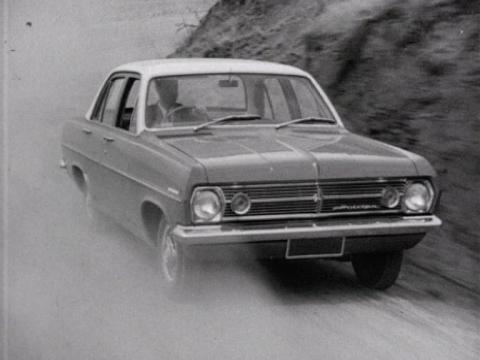 A man drives a Holden car down a dusty road