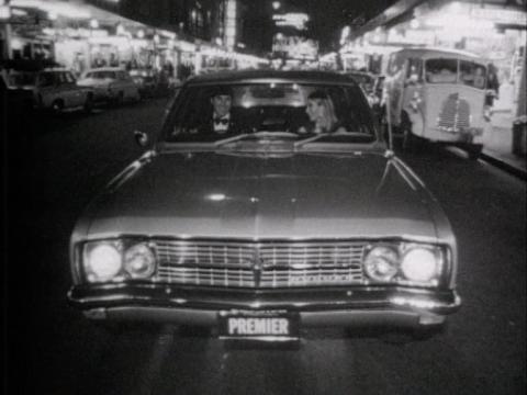 A young couple drive a Holden car down a street at night