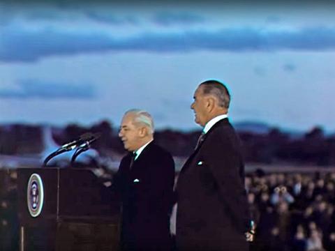 Prime Minister Harold Holt and USA President Lyndon Johnson stand at a podium together in front of a microphone.
