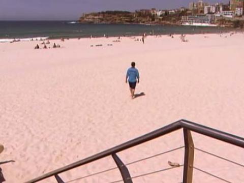 A lifesaver walks across Bondi Beach towards the ocean in a scene from Bondi Rescue