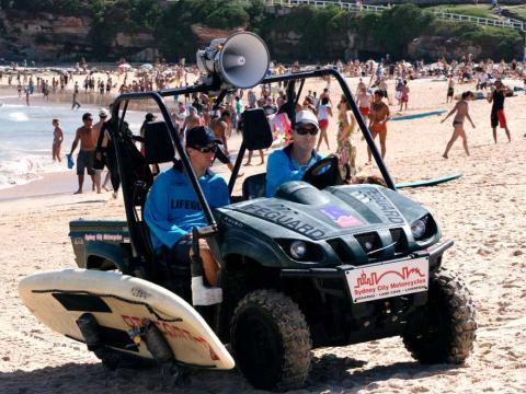 Two lifesavers driving a buggy on a crowded Bondi Beach in a scene from Bondi Rescue