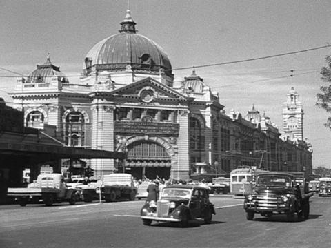Flinders Street Station in Melbourne. Cars are driving past in the foreground. It is a black and white shot.