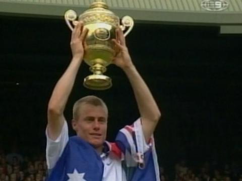 Lleyton Hewitt, draped in an Australian flag, lifts the Wimbledon trophy above his head.