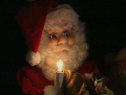 A Santa doll is holding a light that looks like a candle.