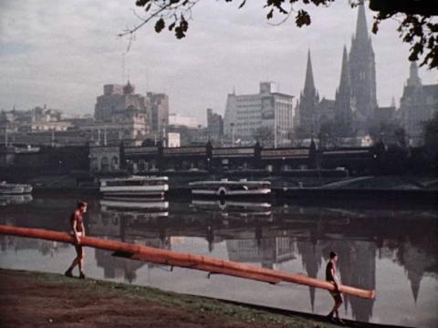 Two men carry a long boat down to the bank of the Yarra River in Melbourne.