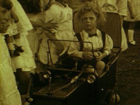 Tinted black and white still of five year-old Wally sitting in his miniature car at his birthday party