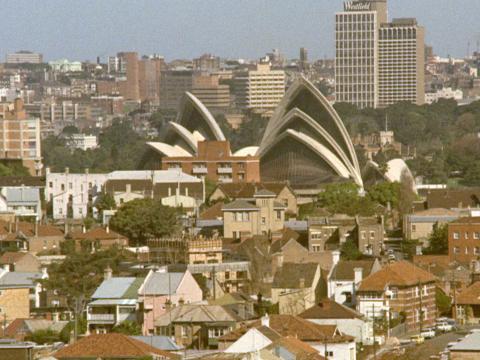 The sails of the Sydney Opera House rising up from in-between a sea of buildings