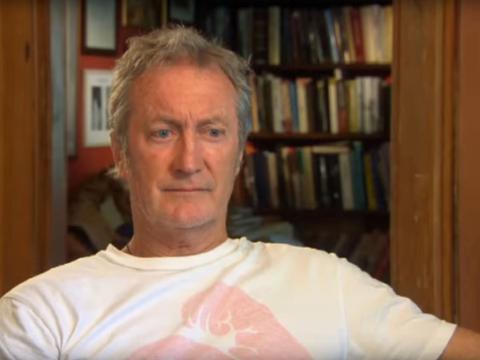 Actor Bryan Brown is being interviewed. He is sitting in a room with bookshelves in the background.