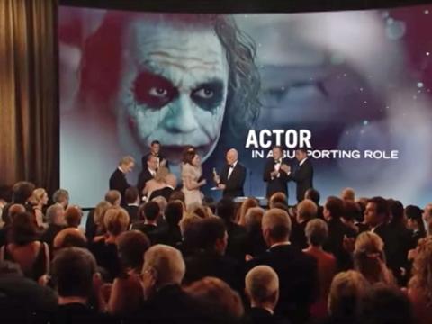 A large screen shows an image of Heath Ledger as The Joker in The Dark Knight. In the foreground Ledger's family go up on stage at the Oscars to accept the award on his behalf.