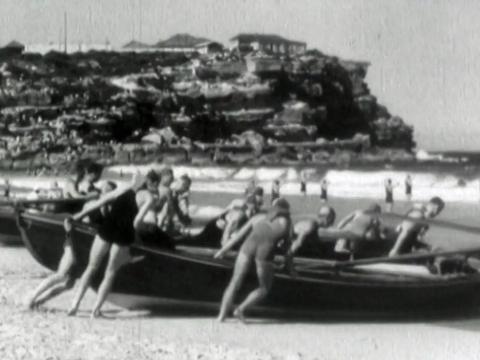 A team of life guards at Bondi Beach pushing rescue boats into the water. 