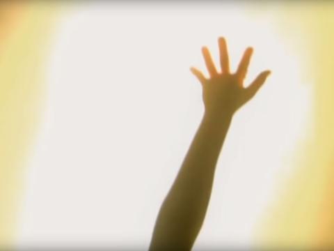 An arm and hand is being held up sillouhetted by bright light.