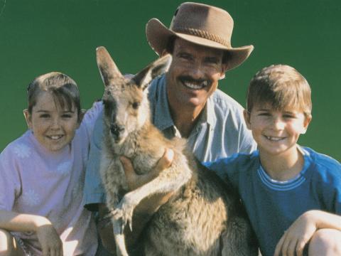 A man with a moustache and hat with a young boy and girl and a kangaroo.